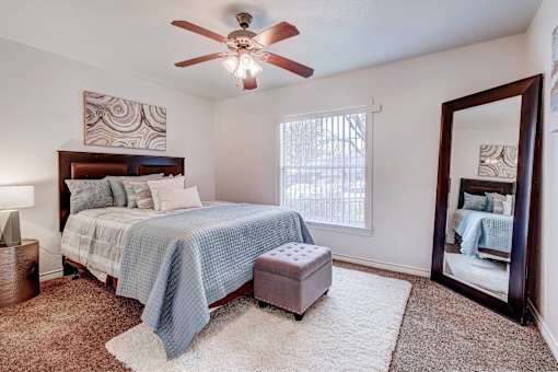 A bedroom with a bed, a ceiling fan, and a mirror.