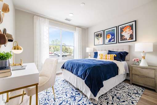 A bedroom with a bed, desk, chair, and pictures on the wall.
