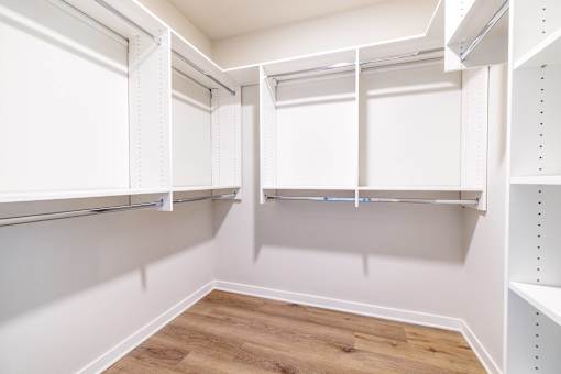 A walk-in closet with white shelving and wooden floors.