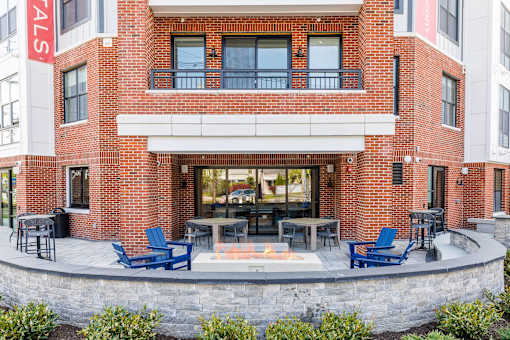 A red brick building with a white awning and blue chairs in front.