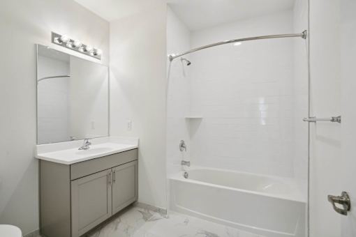 A white bathroom with a sink, mirror, and bathtub.