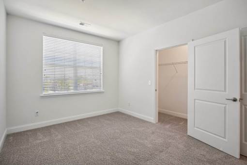 A room with a carpeted floor, a window with blinds, and a door.