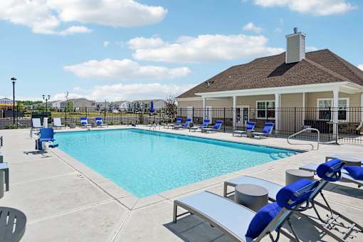 A pool with blue chairs and a house in the background.