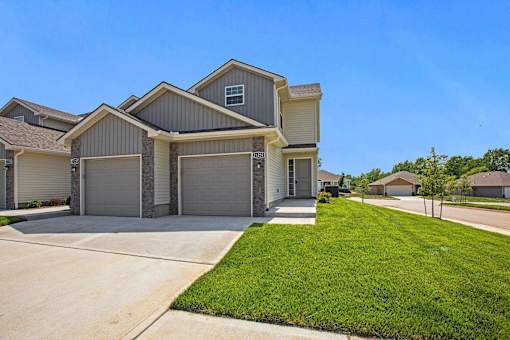 Apartments for Rent Near Spring Hill, KS - Oak Woods - Front Exterior of Townhome with Double Attached Garages, Driveway, and Manicured Lawn.