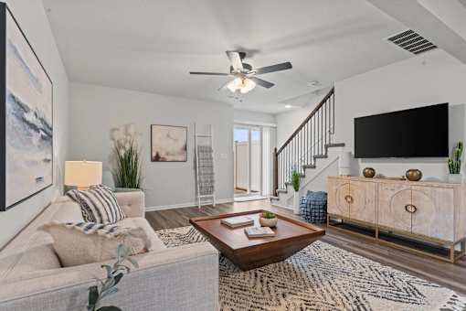 A living room with a grey couch, a coffee table, a staircase, and a flat screen TV.