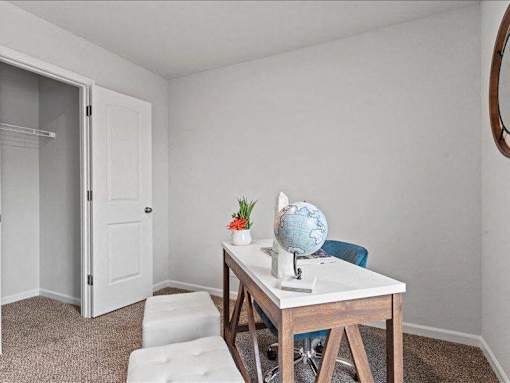 A small table with a globe and flowers on it sits in a corner of a room with a white door and carpeted floor.