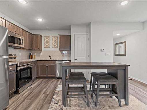 Spring Hill, KS Apartments for Rent - Oak Woods - Kitchen with Plank Flooring, Area Rug, Moveable Island with Stool Seats, Stainless-Steel Appliances, Granite Countertops, and Espresso Cabinetry.