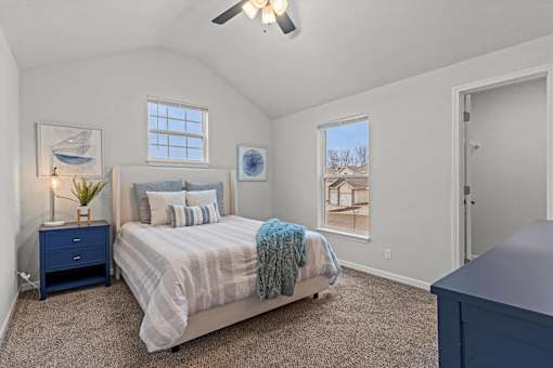 Two-Bedroom Apartments in Spring Hill, KS - Oak Wood - Bedroom with Carpet Flooring, Large Bed, Nightstand with Lamp, Dresser, Vaulted Ceiling, Ceiling Fan, Large Windows, and Spacious Closet.