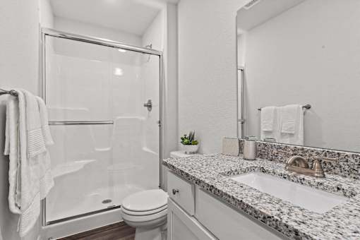 A white bathroom with a marble counter top and a glass shower stall.
