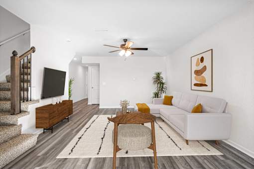 A living room with a white couch, a wooden coffee table, and a staircase.