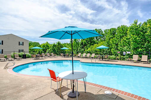 A blue umbrella is next to a table with chairs by a pool.