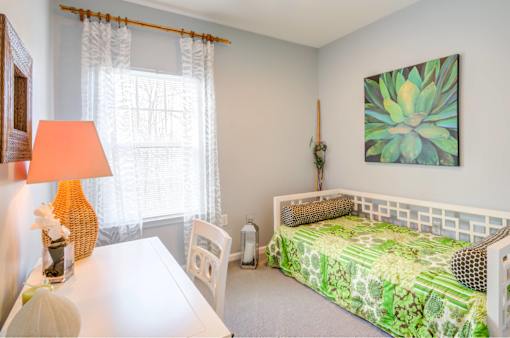 A bedroom with a bed, a table, a chair, a lamp, and a painting on the wall.
