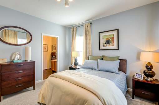 A bedroom with a large bed, a dresser, and a nightstand with a lamp.