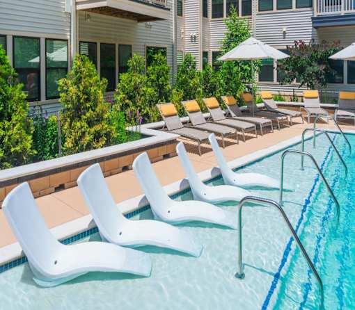 A pool with white chairs and a building in the background.