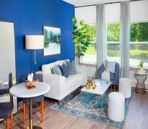 A living room with a white sofa, a round table with a lamp, and a blue rug.