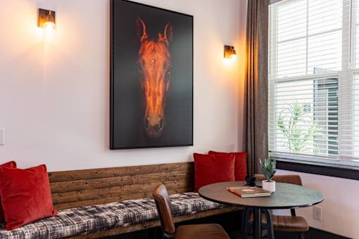 A painting of a horse head is on the wall above a bench with a table and chairs.