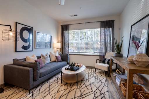 A living room with a grey couch, a coffee table, and a large window with curtains.