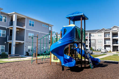 A playground with a blue slide in front of apartment buildings.