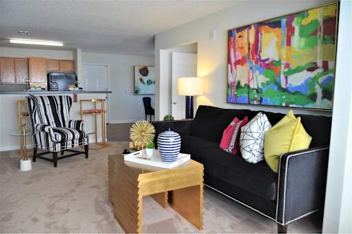 A living room with a black couch and a painting on the wall.
