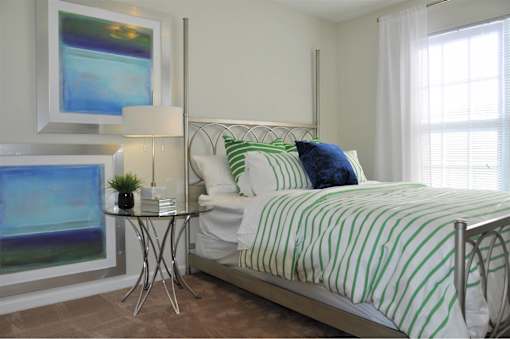 A bedroom with a bed, nightstand, and a painting on the wall.