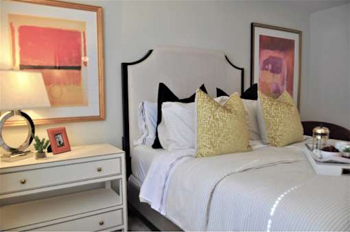 A white bed with a white headboard and a white nightstand with a lamp and a picture frame on it.