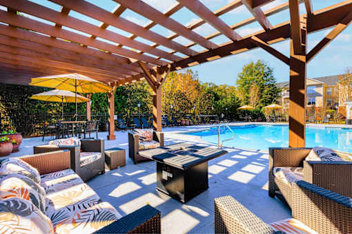 A wooden pergola over a poolside seating area with a yellow umbrella.