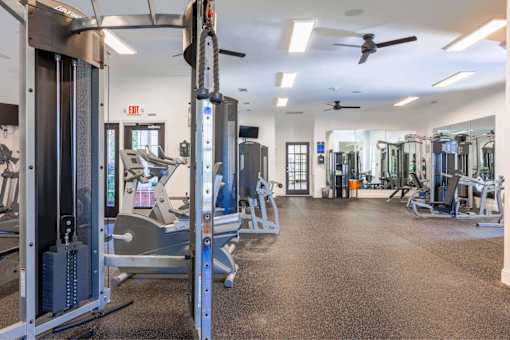 A gym with a variety of equipment including treadmills, weight machines, and a fan.