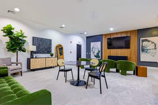 A room with a green couch, a table with chairs, and a plant.