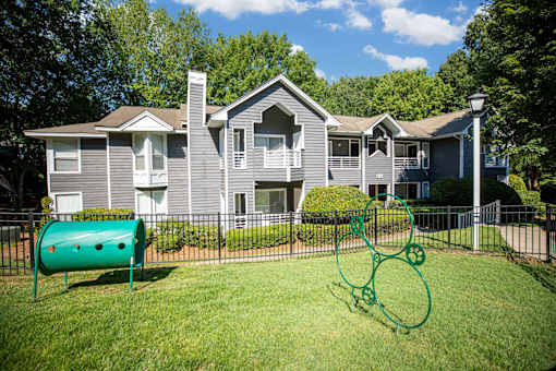 A playground with a green slide and a green climbing frame in front of a grey house.
