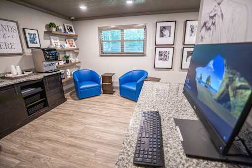 A room with a desk, chairs, and a computer monitor.