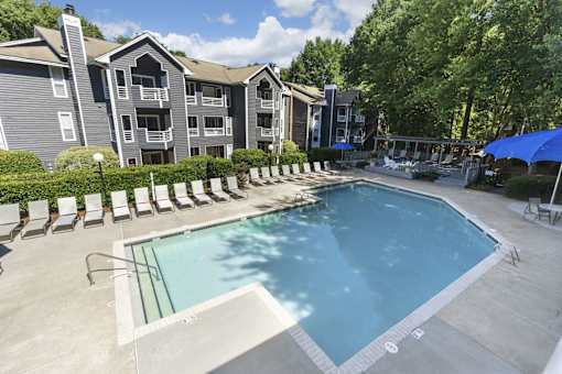 A swimming pool surrounded by lounge chairs and umbrellas in front of apartment buildings.