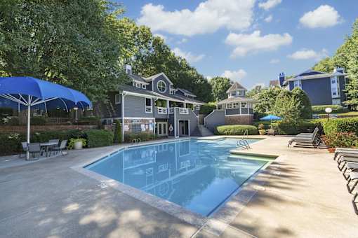 A large swimming pool in front of a house with a blue umbrella.