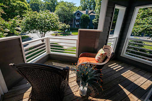 A chair is on a wooden deck with a view of a street and houses.
