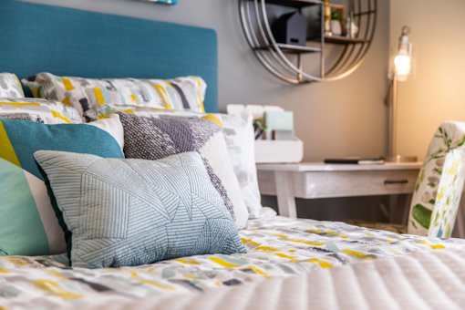 A bed with a blue headboard and a white desk in the background.