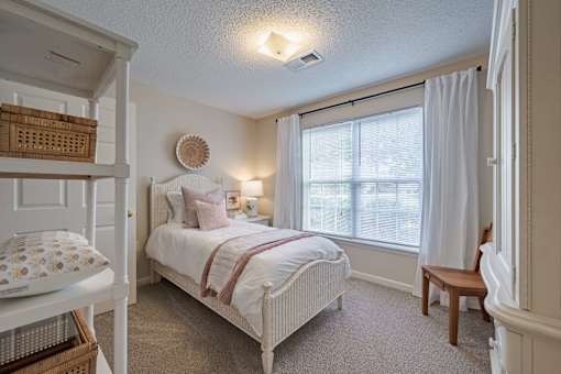 A bedroom with a white bed and a window with white curtains.