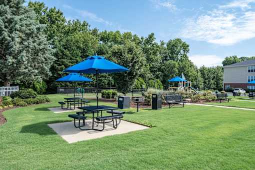 A park with a picnic table and blue umbrellas.
