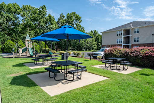 A blue umbrella is over a picnic table in a grassy area.