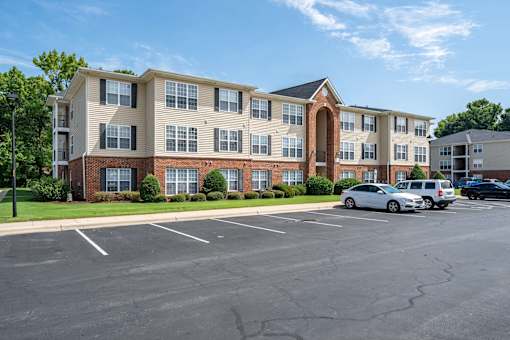 A parking lot in front of a two-story apartment building with a white car parked in the lot.