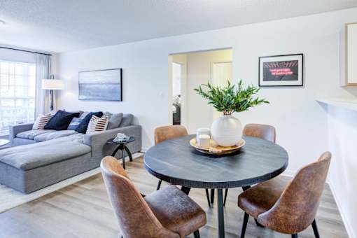 A living room with a grey couch, a round table with a vase on it, and a plant in the corner.