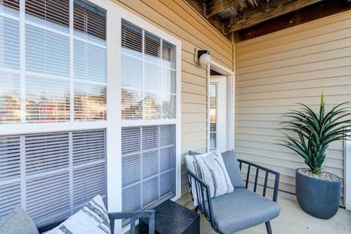 A chair with a cushion and a potted plant are on a porch.
