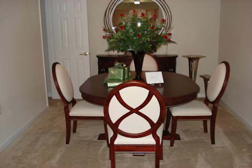 A brown table with a vase of flowers and chairs around it.