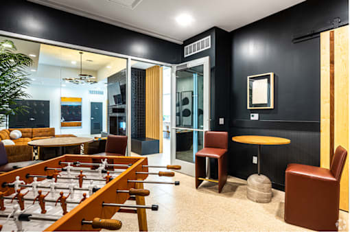 A foosball table is in the middle of a room with black walls and a glass door.