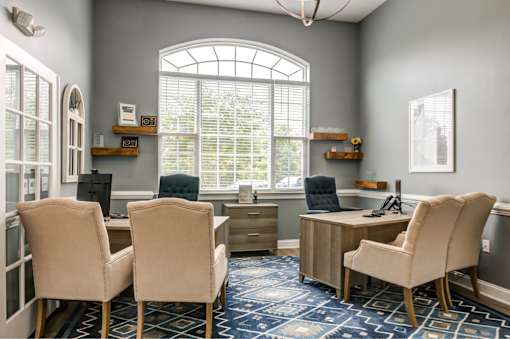 A room with a desk and chairs with a window in the background.