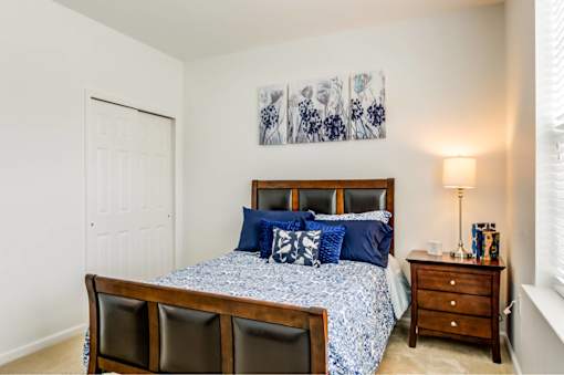 A bedroom with a bed, two chairs, and a nightstand.
