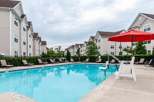 A red umbrella is on the right side of a pool.