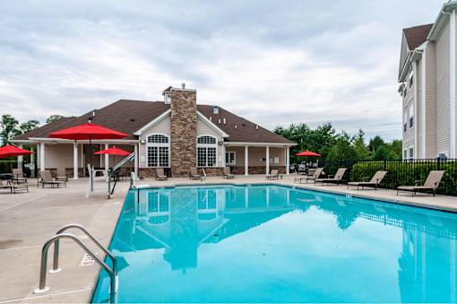 A large swimming pool in front of a house with a stone chimney.