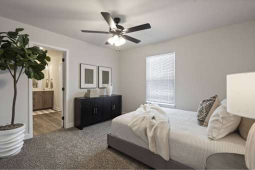 A bedroom with a bed, a ceiling fan, and a potted plant.