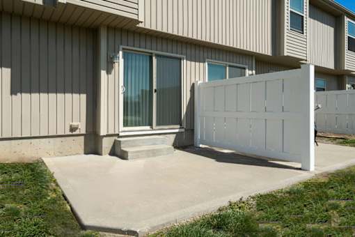 Peculiar, MO, Townhomes - Bradley’s Crossing - Outdoor Patio with Yard, Concrete Flooring, White Fence, and Grass Area.