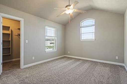 A room with a ceiling fan and two windows.