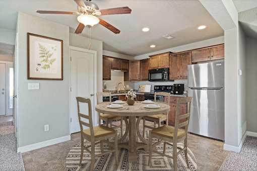 Townhomes for Rent in Peculiar, MO - Bradley’s Crossing - Dining Room with High Ceiling, Ceiling Fan with Light, Vinyl Plank Flooring, 4-Seater Dining Table and Chairs, Round Rug, and Wall Art.